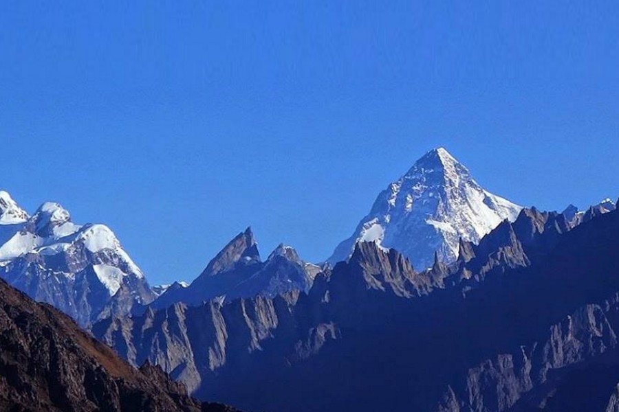 Hiker standing on a rocky peak with trekking poles, overlooking a breathtaking mountain landscape.