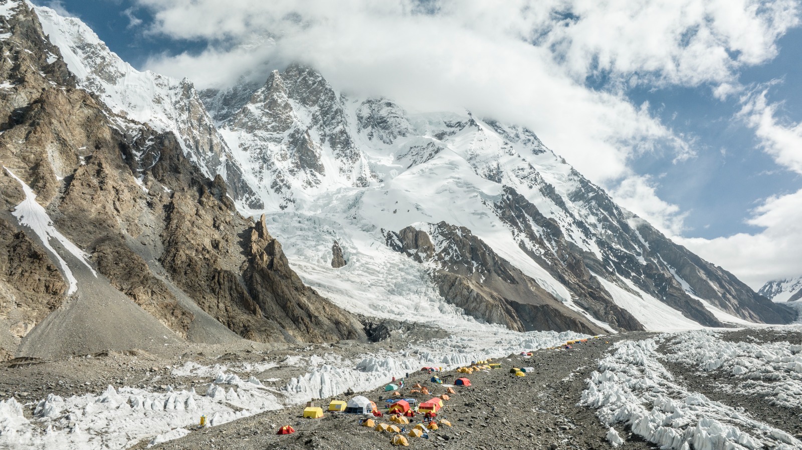 A scenic view of a high-altitude base camp with colorful tents set against the backdrop of snow-covered peaks in the Karakoram range.