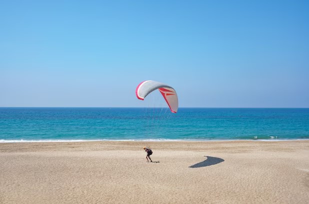Paragliding Over the Beach – A person soaring with a parachute over a sandy beach